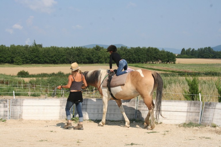 une monitrice apprend à une enfant la voltige à cheval pendant une colo été